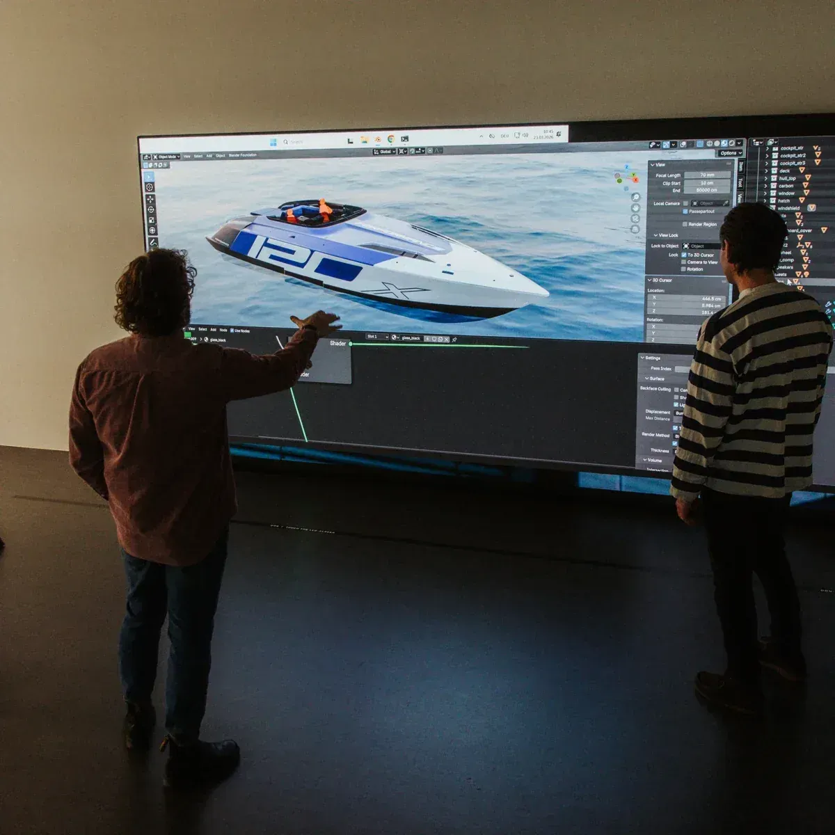 Zwei Männer vor einer Großbildleinwand, auf der das 3D-Modell eines Rennboots in einer Design-Software zu sehen ist