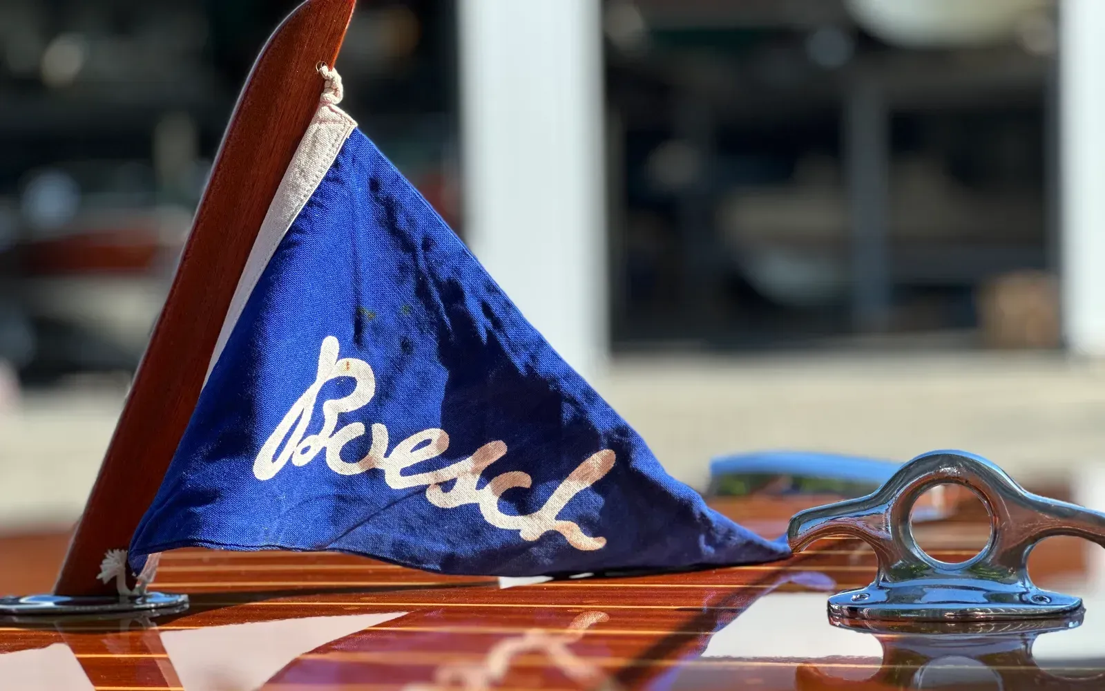 Handpoliertes Mahagoni-Deck eines klassischen Motorboots mit blauem Werft-Stander und verchromter Klampe
