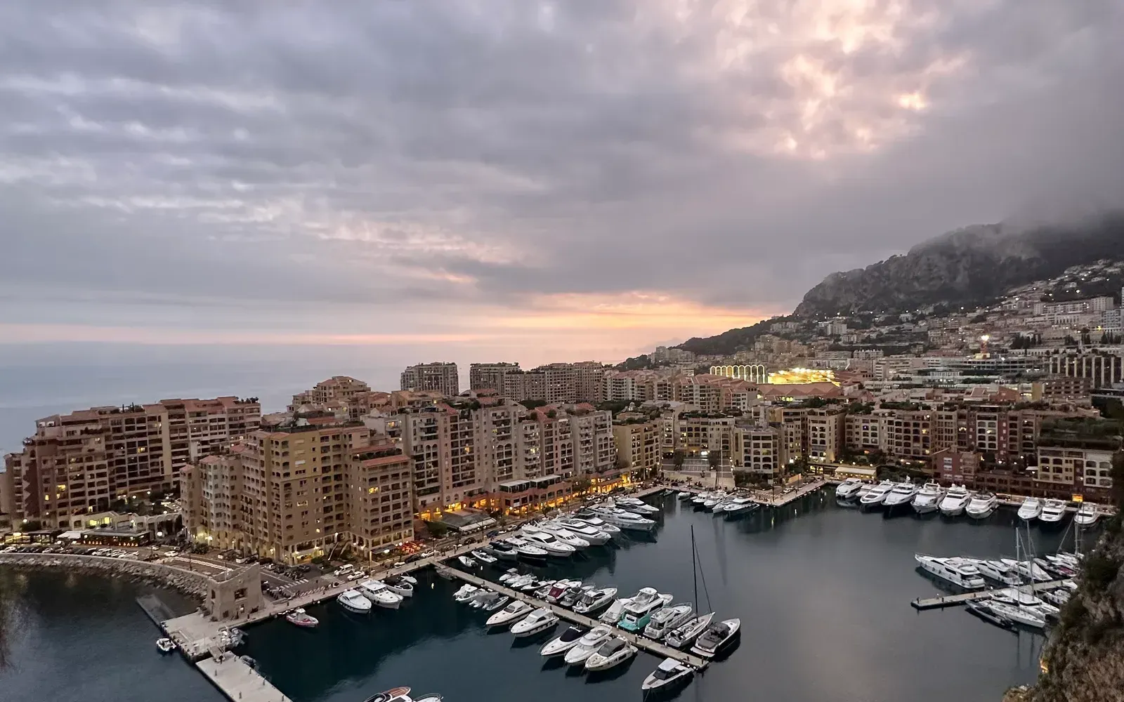 Yachthafen von Monaco in der Abenddämmerung — Motoryachten an den Stegen vor beleuchteter Stadtkulisse
